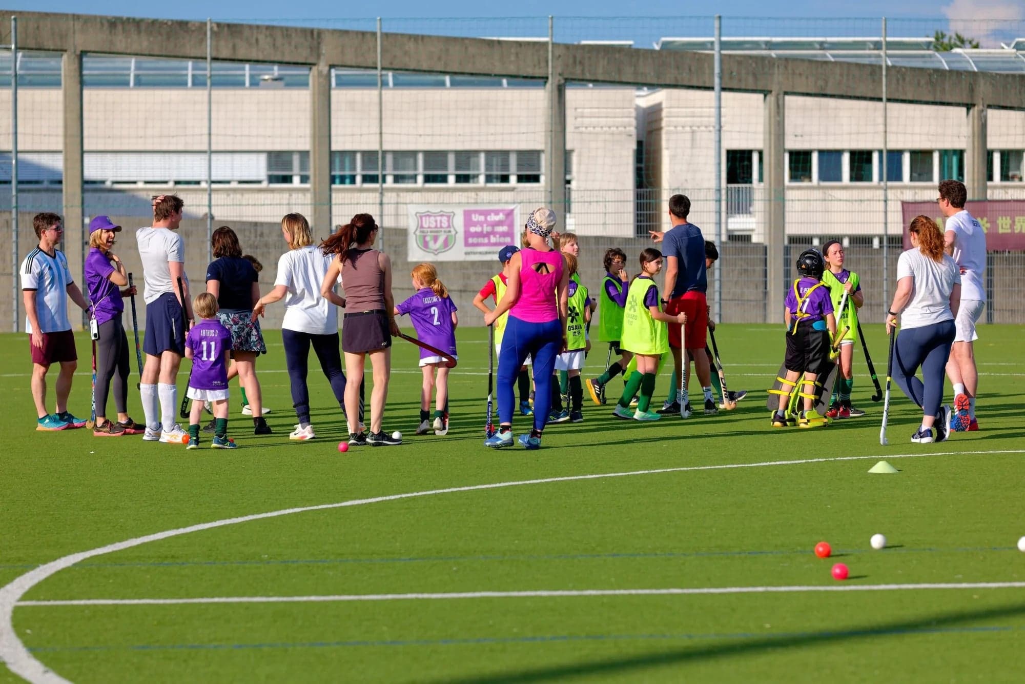 Young USTS players, their coaches and parents with their sticks on the club's pitch, the club's banner on the fence behind them.